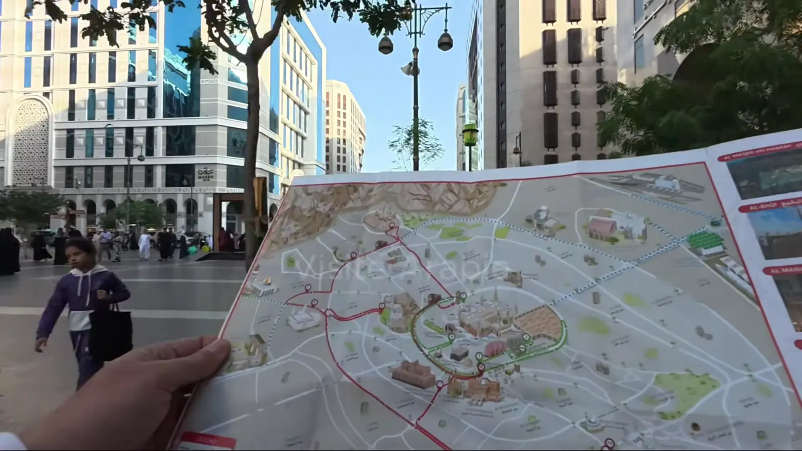 La carte du parcours du bus des visites de Médine, dépliée dans les mains, près de la mosquée du Prophète