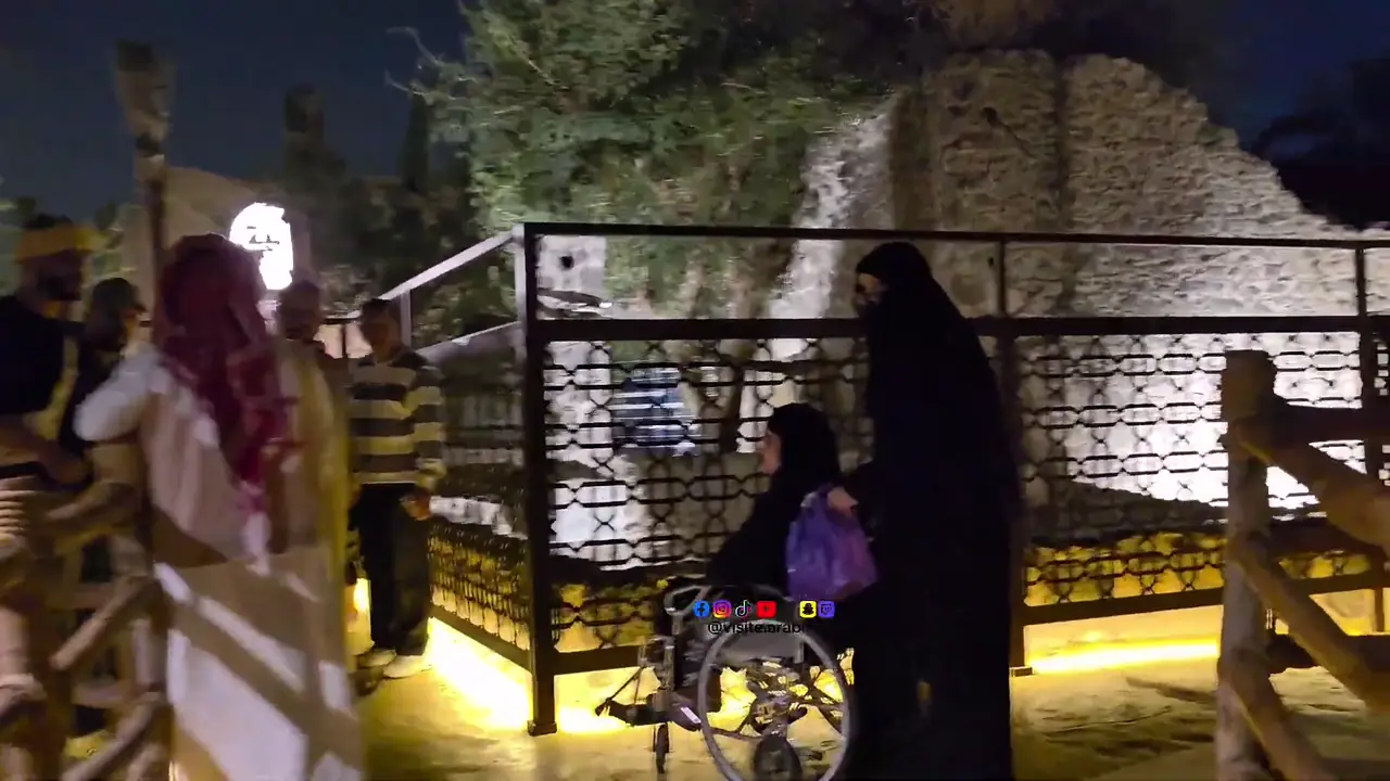 Le puits historique éclairé dans la palmeraie d'arrivée de Qubâʾ, avec une visiteuse en fauteuil roulant